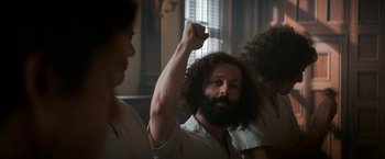 Movie still from “The Trial of the Chicago 7” (2020), directed by Aaron Sorkin – A man with long hair and a beard raising his fist in the air; Medium shot, Low angle