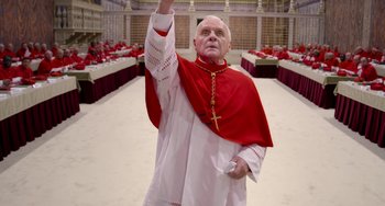 Movie still from “The Two Popes” (2019), directed by Fernando Meirelles – A man dressed as a priest holding up his hand; Medium shot, Low angle