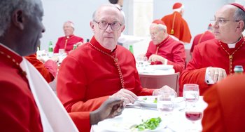Movie still from “The Two Popes” (2019), directed by Fernando Meirelles – A group of men sitting at a table with plates of food on it; Medium shot, Over the shoulder angle