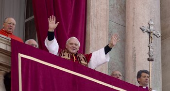 Movie still from “The Two Popes” (2019), directed by Fernando Meirelles – An older man in a red and white outfit waves to the crowd from a balcony; Medium shot, Low angle