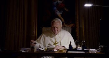 Movie still from “The Two Popes” (2019), directed by Fernando Meirelles – An older man sitting at a desk with a painting behind him; Medium shot, High angle