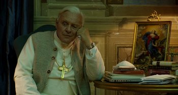 Movie still from “The Two Popes” (2019), directed by Fernando Meirelles – An older man sitting at a table with a cell phone to his ear; Medium shot, High angle