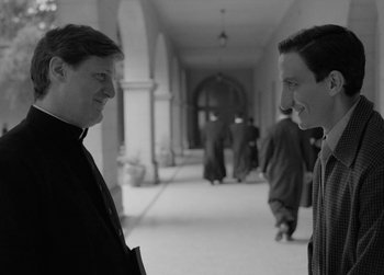 Movie still from “The Two Popes” (2019), directed by Fernando Meirelles – Two men are standing in a hallway and talking to each other; Medium shot, Over the shoulder angle