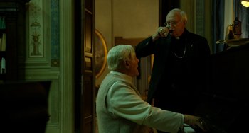 Movie still from “The Two Popes” (2019), directed by Fernando Meirelles – Two older men are drinking wine in a room; Medium shot, Over the shoulder angle