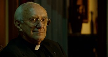 Movie still from “The Two Popes” (2019), directed by Fernando Meirelles – An older man wearing glasses and a priest's outfit; Close Up shot, Over the shoulder angle