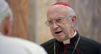 Movie still from “The Two Popes” (2019), directed by Fernando Meirelles – An older man wearing glasses and wearing a red hat; Close Up shot, Over the shoulder angle