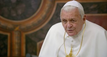 Movie still from “The Two Popes” (2019), directed by Fernando Meirelles – An older man wearing a white outfit and a gold cross; Close Up shot, Over the shoulder angle