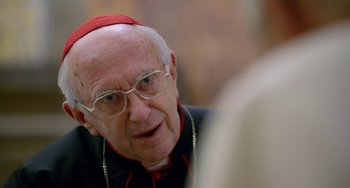 Movie still from “The Two Popes” (2019), directed by Fernando Meirelles – An older man wearing glasses and wearing a red hat; Close Up shot, Over the shoulder angle