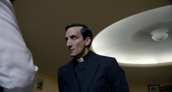 Movie still from “The Two Popes” (2019), directed by Fernando Meirelles – A man in a priest's outfit stands in front of a light; Medium shot, Low angle