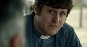 Movie still from “The Two Popes” (2019), directed by Fernando Meirelles – A man in a priest's outfit looking at the camera; Close Up shot, Over the shoulder angle