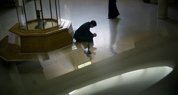 Movie still from “The Two Popes” (2019), directed by Fernando Meirelles – A man sitting on the ground looking at his cell phone; Wide shot, High angle
