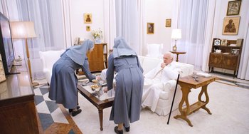 Movie still from “The Two Popes” (2019), directed by Fernando Meirelles – A group of nuns in a room with a man sitting on a couch; Wide shot, High angle