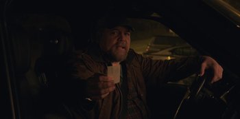Movie still from “The Unforgivable” (2021), directed by Nora Fingscheidt – A man in a brown jacket holding up a white device; Close Up shot, Over the shoulder angle