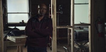 Movie still from “The Unforgivable” (2021), directed by Nora Fingscheidt – A man standing in front of a wooden structure; Medium shot, Low angle