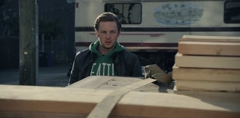 Movie still from “The Unforgivable” (2021), directed by Nora Fingscheidt – A man sitting in front of a wooden table; Medium shot, Over the shoulder angle