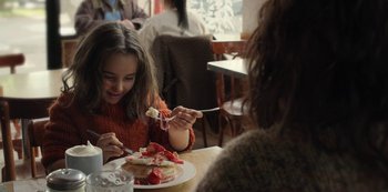 Movie still from “The Unforgivable” (2021), directed by Nora Fingscheidt – A woman and a girl eating cake at a table; Medium shot, Over the shoulder angle