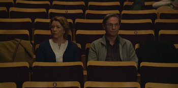Movie still from “The Unforgivable” (2021), directed by Nora Fingscheidt – A man and a woman are sitting in a row of seats; Medium shot, High angle