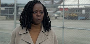 Movie still from “The Unforgivable” (2021), directed by Nora Fingscheidt – A woman with dreads standing in front of a chain link fence; Close Up shot, Over the shoulder angle