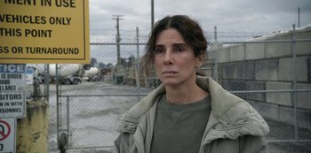 Movie still from “The Unforgivable” (2021), directed by Nora Fingscheidt – A woman standing in front of a chain link fence; Close Up shot, High angle