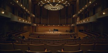Movie still from “The Unforgivable” (2021), directed by Nora Fingscheidt – Two people are playing piano in an auditorium; Extreme Wide shot, High angle