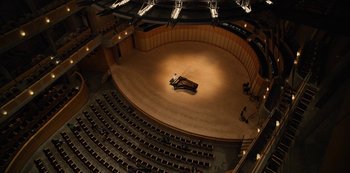 Movie still from “The Unforgivable” (2021), directed by Nora Fingscheidt – An auditorium with a grand piano on the stage; Extreme Wide shot, High angle