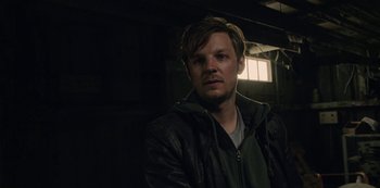 Movie still from “The Unforgivable” (2021), directed by Nora Fingscheidt – A man in a green jacket is in a dark room; Close Up shot, Over the shoulder angle