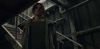 Movie still from “The Unforgivable” (2021), directed by Nora Fingscheidt – A woman standing in front of a wooden staircase; Medium shot, Low angle