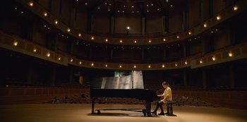 Movie still from “The Unforgivable” (2021), directed by Nora Fingscheidt – A man sitting at a grand piano in an auditorium; Extreme Wide shot, High angle