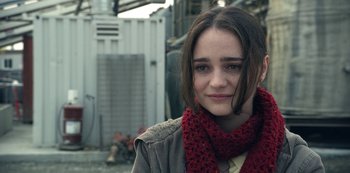 Movie still from “The Unforgivable” (2021), directed by Nora Fingscheidt – A young woman wearing a red scarf and a gray jacket; Close Up shot, Over the shoulder angle