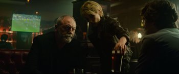 Movie still from “The Vault” (2021), directed by Jaume Balagueró – A man and a woman in a room with drinks; Medium shot, Over the shoulder angle