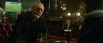 Movie still from “The Vault” (2021), directed by Jaume Balagueró – An older man sitting at a table with a glass of beer in front of him; Medium shot, Over the shoulder angle