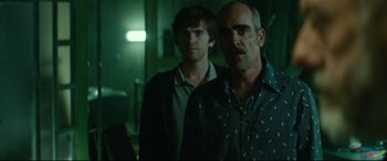 Movie still from “The Vault” (2021), directed by Jaume Balagueró – Two men standing next to each other in a dark room; Medium shot, Over the shoulder angle