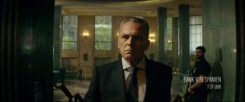Movie still from “The Vault” (2021), directed by Jaume Balagueró – A man in a suit and tie in a room; Medium shot, Low angle