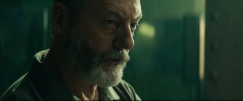Movie still from “The Vault” (2021), directed by Jaume Balagueró – An older man with a beard looking into the distance; Close Up shot, Over the shoulder angle