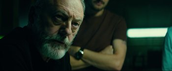 Movie still from “The Vault” (2021), directed by Jaume Balagueró – A man with a beard is looking at the camera with another man standing behind him; Close Up shot, Over the shoulder angle
