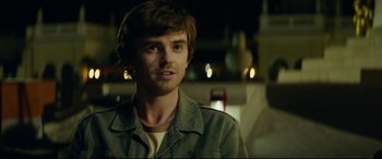 Movie still from “The Vault” (2021), directed by Jaume Balagueró – A young man with long brown hair wearing a green jacket; Close Up shot, Over the shoulder angle