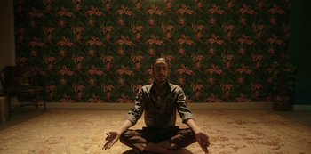 Movie still from “The White Tiger” (2021), directed by Ramin Bahrani – A man sitting on the ground in a yoga pose; Medium shot, High angle