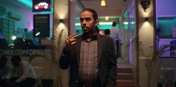 Movie still from “The White Tiger” (2021), directed by Ramin Bahrani – A man in a black jacket and a red and black shirt; Medium shot, Low angle