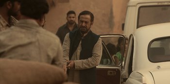 Movie still from “The White Tiger” (2021), directed by Ramin Bahrani – A man shaking hands with another man in front of a car; Medium shot, Over the shoulder angle