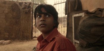 Movie still from “The White Tiger” (2021), directed by Ramin Bahrani – A young man wearing a red shirt looking to his left; Close Up shot, Low angle