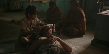 Movie still from “The White Tiger” (2021), directed by Ramin Bahrani – An old man is laying on the ground while a group of people watch; Medium shot, High angle