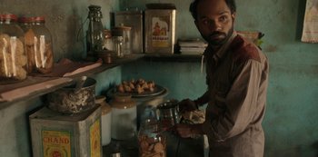 Movie still from “The White Tiger” (2021), directed by Ramin Bahrani – A man standing in front of an oven in a kitchen; Medium shot, High angle