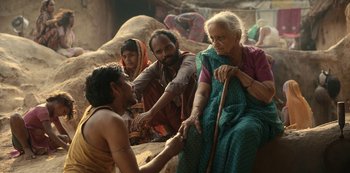 Movie still from “The White Tiger” (2021), directed by Ramin Bahrani – A group of people gathered around a man with a cane; Medium shot, Over the shoulder angle