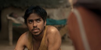 Movie still from “The White Tiger” (2021), directed by Ramin Bahrani – A man with a beard is looking at the camera; Close Up shot, Over the shoulder angle