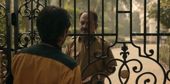 Movie still from “The White Tiger” (2021), directed by Ramin Bahrani – Two men are standing in front of a gate; Medium shot, Over the shoulder angle