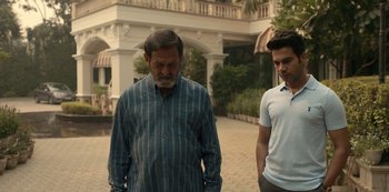 Movie still from “The White Tiger” (2021), directed by Ramin Bahrani – Two men standing next to each other in front of a building; Medium shot, Over the shoulder angle