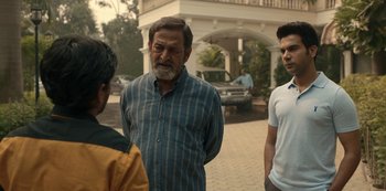 Movie still from “The White Tiger” (2021), directed by Ramin Bahrani – Three men standing in front of a building; Medium shot, Over the shoulder angle
