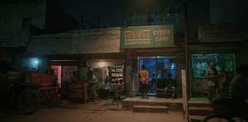 Movie still from “The White Tiger” (2021), directed by Ramin Bahrani – A group of people sitting outside of a computer cafe; Extreme Wide shot, Low angle