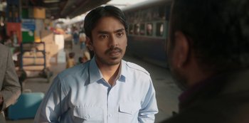 Movie still from “The White Tiger” (2021), directed by Ramin Bahrani – A man standing in front of a train on a train platform; Close Up shot, Over the shoulder angle