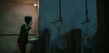 Movie still from “The White Tiger” (2021), directed by Ramin Bahrani – A man is taking a picture of himself in a bathroom; Medium shot, Low angle